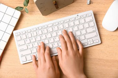 Dişi programcı, tahta zemin üzerinde saat, fare ve defter kullanan bilgisayar klavyesi kullanıyor