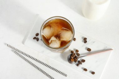 Bir bardak buzlu kahve, süt şişesi, fasulye ve pipet beyaz grunge arka planda.