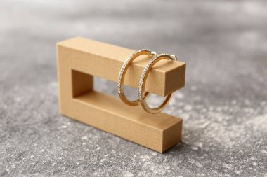 Gri arka planda altın küpeleri olan dekoratif bir podyum.