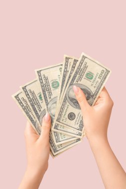 Pembe arka planda 100 dolarlık banknotlar tutan kadın eller.