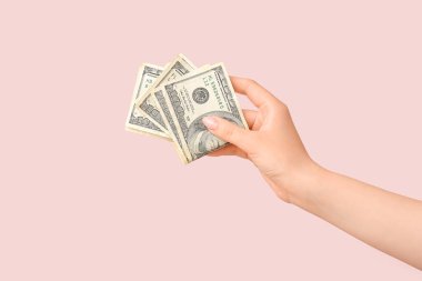 Pembe arka planda 100 dolarlık banknotlar tutan kadın.