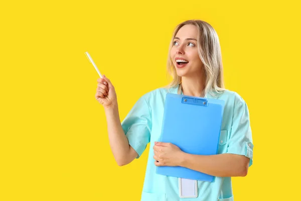 带剪贴板的女实习医生指着黄色背景的东西 — 图库照片