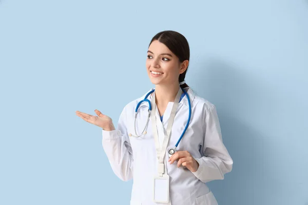 青い背景に何かを示す聴診器を持つ女性医師 — ストック写真