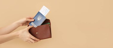 Kadın Ukrayna pasaportu ve bileti, bej arka planda, metin için yeri olan cüzdana koyuyor.