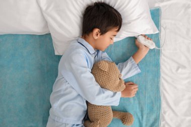 Little boy with toy sleeping on electric heating pad in bedroom