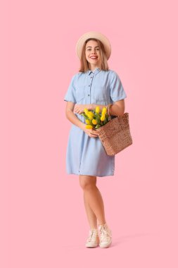 Young woman in hat with bag of tulips on pink background