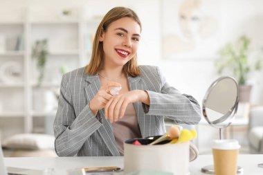 Makyaj vakfını evinde eline süren genç bir kadın.