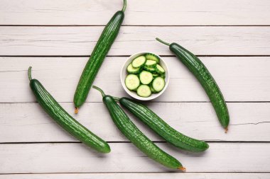 Kesilmiş kase ve açık ahşap arka planda salatalıklar.