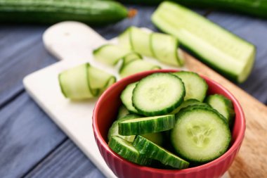 Gri ahşap arka planda taze kesilmiş salatalıklı kase, yakın plan.