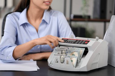 Kadın banka müdürü ofiste para sayma makinesi kullanıyor, yakın plan.