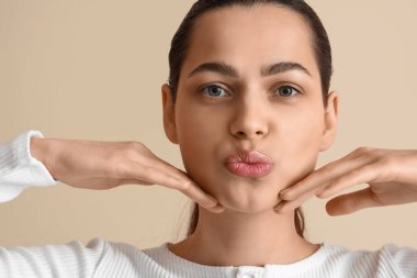 Bej arka plan üzerinde yüz geliştirme egzersizi yapan genç kadın, yakın plan.