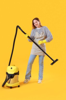 Sarı arka planda elektrik süpürgesi olan genç bir kadın.