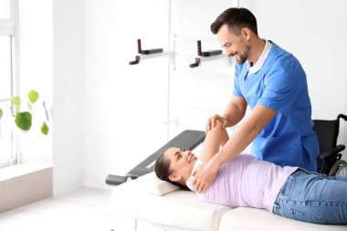 Rehabilitasyon merkezinde genç bir kadınla çalışan erkek fizyoterapist.