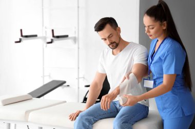 Rehabilitasyon merkezindeki genç adamın koluna bandaj uygulayan kadın fizyoterapist.