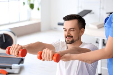 Genç adam rehabilitasyon merkezinde dambıl ve fizyoterapist eğitimi alıyor.