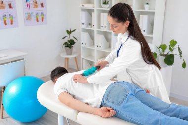 Kadın fizyoterapist rehabilitasyon merkezinde genç adama masaj yapıyor.