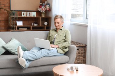 Evde dizüstü bilgisayarla çalışan olgun bir kadın serbest yazar.