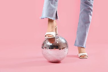 Pembe arka planda disko topu olan şık bir kadının bacakları.