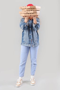 Kadın kurye gri arka planda bir sürü pizza kutusu tutuyor.