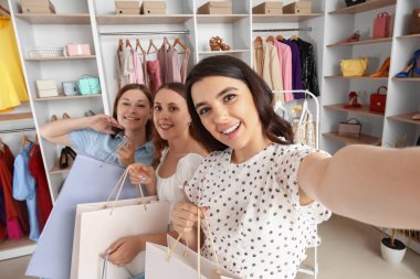 Alışveriş torbalı genç kadınlar dükkânda selfie çekiyorlar.