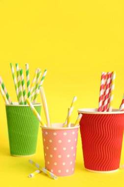 Sarı arka planda farklı pipetli kağıt bardaklar.