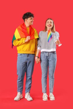 Kırmızı arka planda el ele tutuşan LGBT bayraklı genç çift