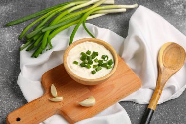 Lezzetli ekşi krema ve gri arka planda dilimlenmiş yeşil soğan tabağı.