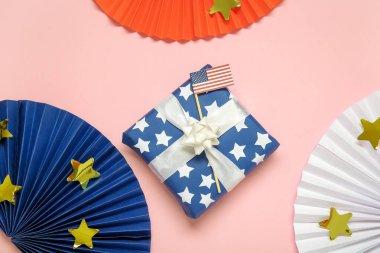 Üzerinde ABD bayrağı olan bir hediye kutusu ve pembe arka planda renkli hayranlar. Amerikan Bağımsızlık Günü