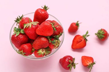 Pembe arka planda taze çilekli cam kase.