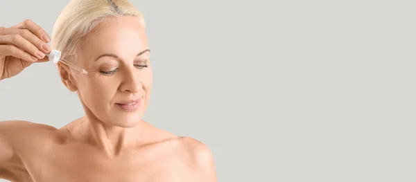 Gammal Blond Kvinna Applicera Serum Hennes Ansikte Mot Ljus Bakgrund — Stockfoto