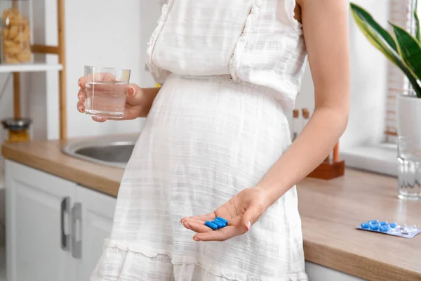 若いです妊娠中の女性とともにガラスの水と葉酸の丸薬でキッチン クローズアップ — ストック写真