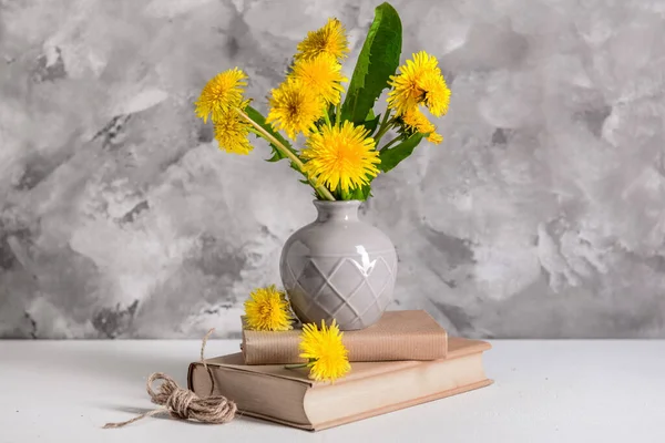 Vase with beautiful dandelion flowers, books and rope on light table against grunge background