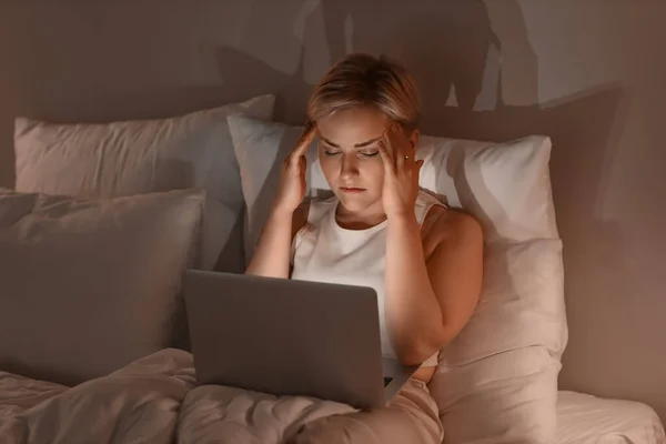 stock image Sleepy young woman using laptop in bed at night