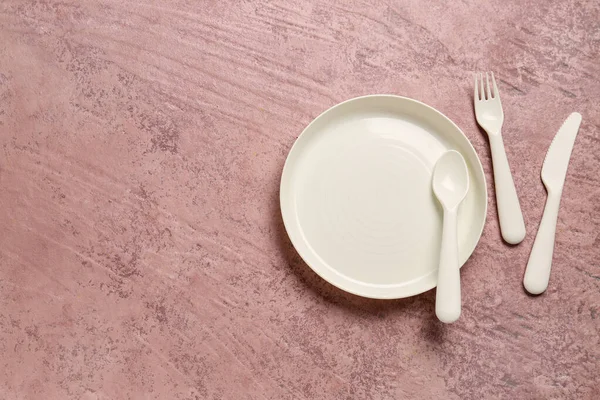 Plate with eating utensils for baby on grunge pink background