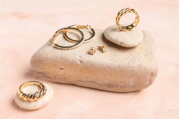 粉色背景上有漂亮戒指和耳环的石头 — 图库照片