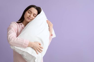 Young woman with soft pillow on lilac background