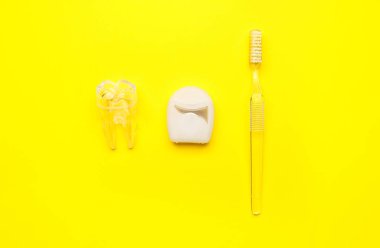 Diş ipi, plastik diş modeli ve sarı arka planda fırça.