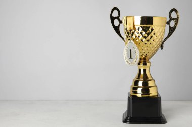 Altın kupa, gri duvarın yanındaki masada birincilik madalyası.