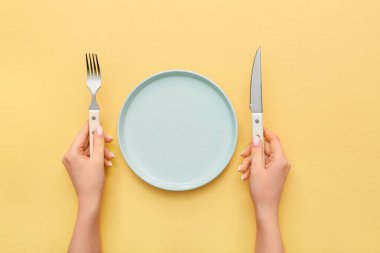 Çatal bıçaklı ve sarı masadaki boş tabaklı kadın elleri.