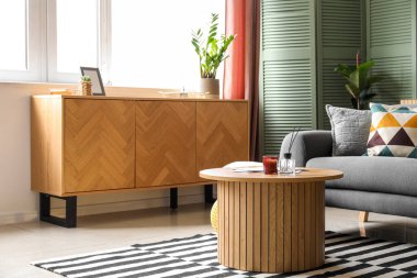 Işıl ışıl oturma odasının içi rahat gri kanepe, sehpa ve ahşap dolap.