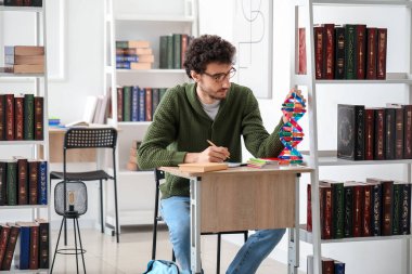 Erkek öğrenci kütüphanede DNA modeliyle çalışıyor.