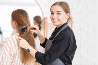 Güzellik salonunda genç bir kadının saçını tarayan kadın kuaför.