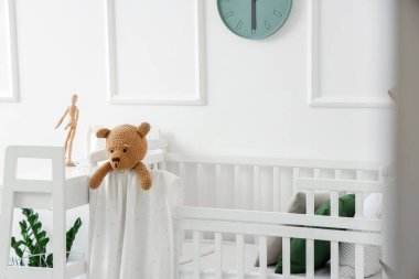 Baby crib with toy bear in light bedroom