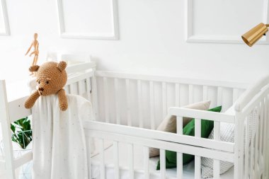 Baby crib with toy bear in light bedroom