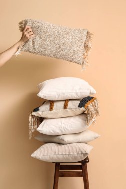 Kadın bej duvarın yanındaki tabureden yastık alıyor.