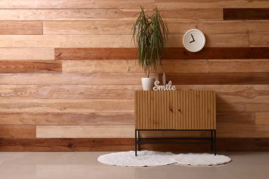 Odanın ahşap duvarının yanında içi palmiye ağacı ve dekor dolu çekmeceler.