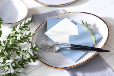 Şık masa ayarları, boş kartlı zarf ve beyaz karo arka planda ağaç dalları