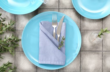 Katlanmış peçete, çatal bıçak takımı ve gri fayanslı bitki dalı olan tabaklar.