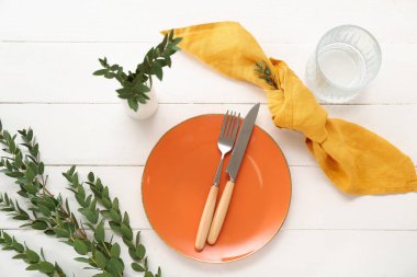 Katlanmış peçete, çatal bıçak takımı ve beyaz ahşap arka planda cam tabaklar.