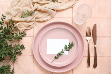 Çatal bıçaklı tabaklar, boş kart ve pembe fayanslı cam.